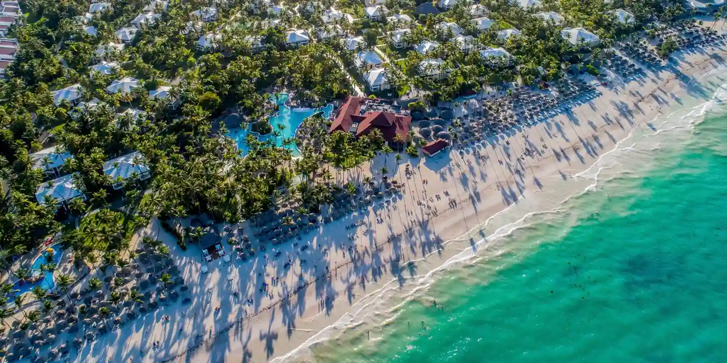 Vista panor&aacute;mica del hotel en las playas de Punta Cana con arena blanca, palmeras y sillas